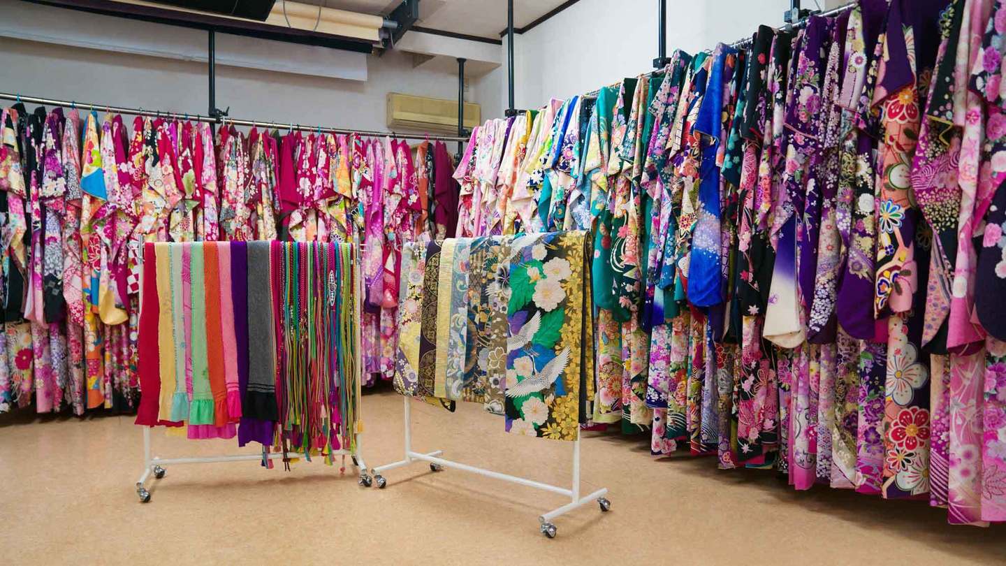 三原市・冨士写真館の広々とした振袖展示スペース。古典柄からモダンまで豊富な品揃えの振袖と、色とりどりの帯締め・帯揚げが並ぶ店内の様子。