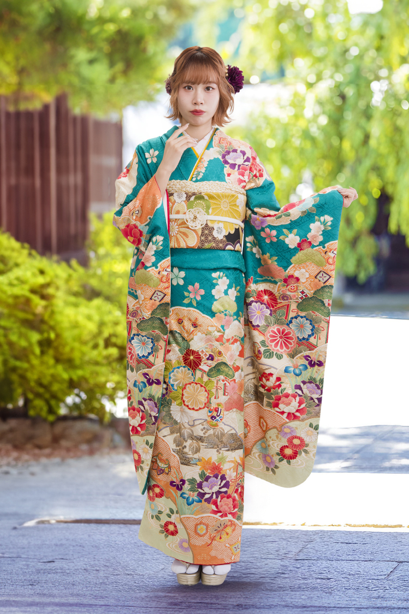 鮮やかなエメラルドグリーンにオレンジや金の道長取りが映える、晴れやかな古典柄振袖。成人式会場に色彩豊かな花々が輝く、二十歳の若々しさと躍動感あふれる装い。
