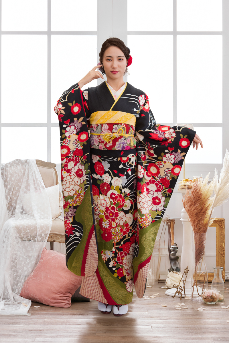 黒地に赤や白の大輪の牡丹が咲き誇り、鮮やかなグリーンの道長取りがアクセントになったレトロモダンな振袖。黄色の小物を効かせた、個性的で華やかな二十歳の装い。