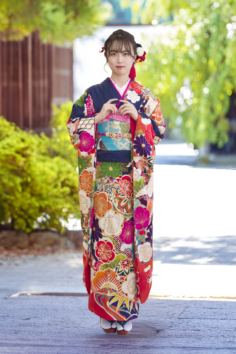 趣ある屋外ロケーションに映える濃紺の振袖。鮮やかな赤やオレンジの古典花が咲き誇る華やかなデザインで、伝統美と若々しさを兼ね備えた成人式の装い。